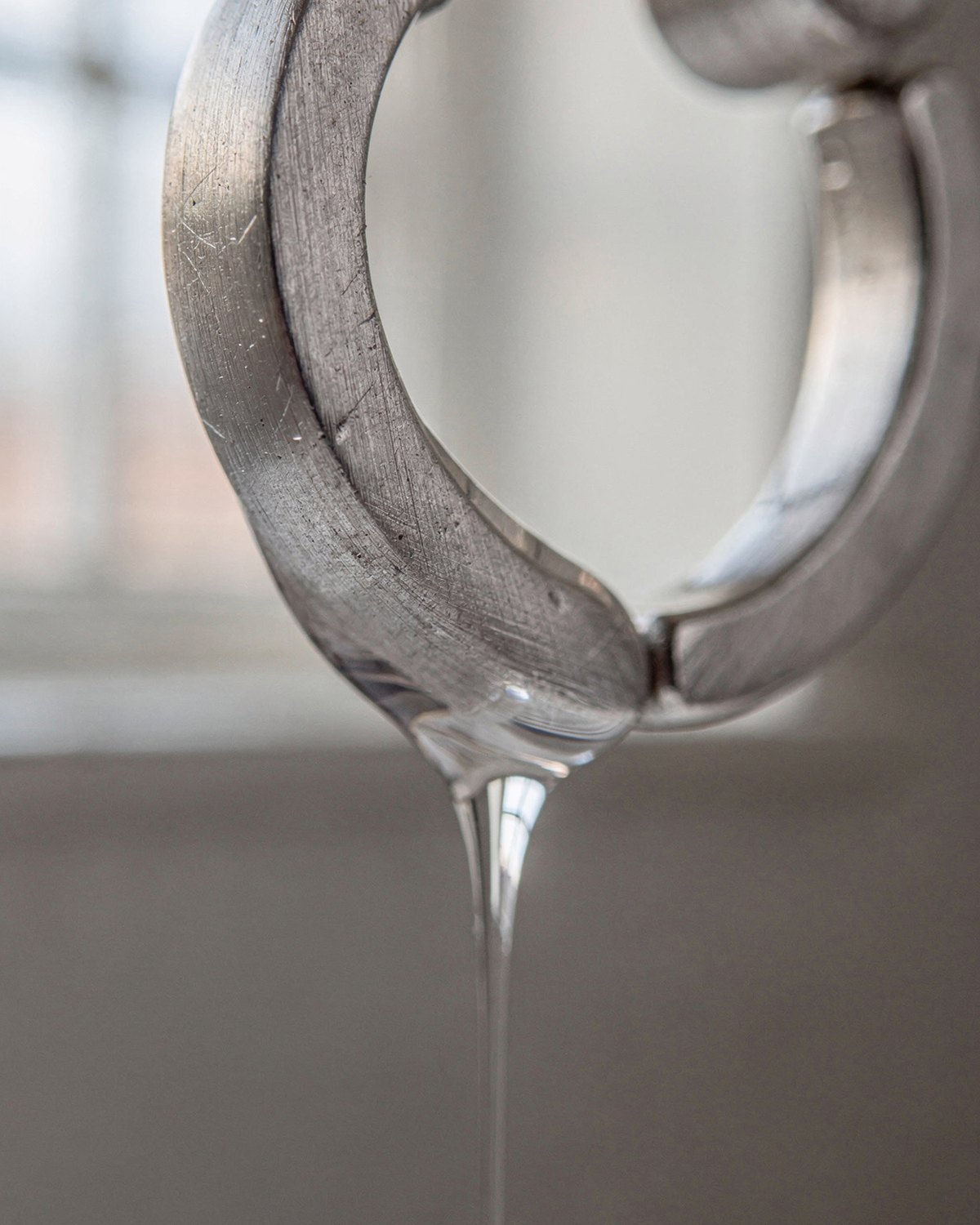 Macro sur une créole en argent sterling 925 : une goutte d’eau glisse le long du métal et le quitte par le bas