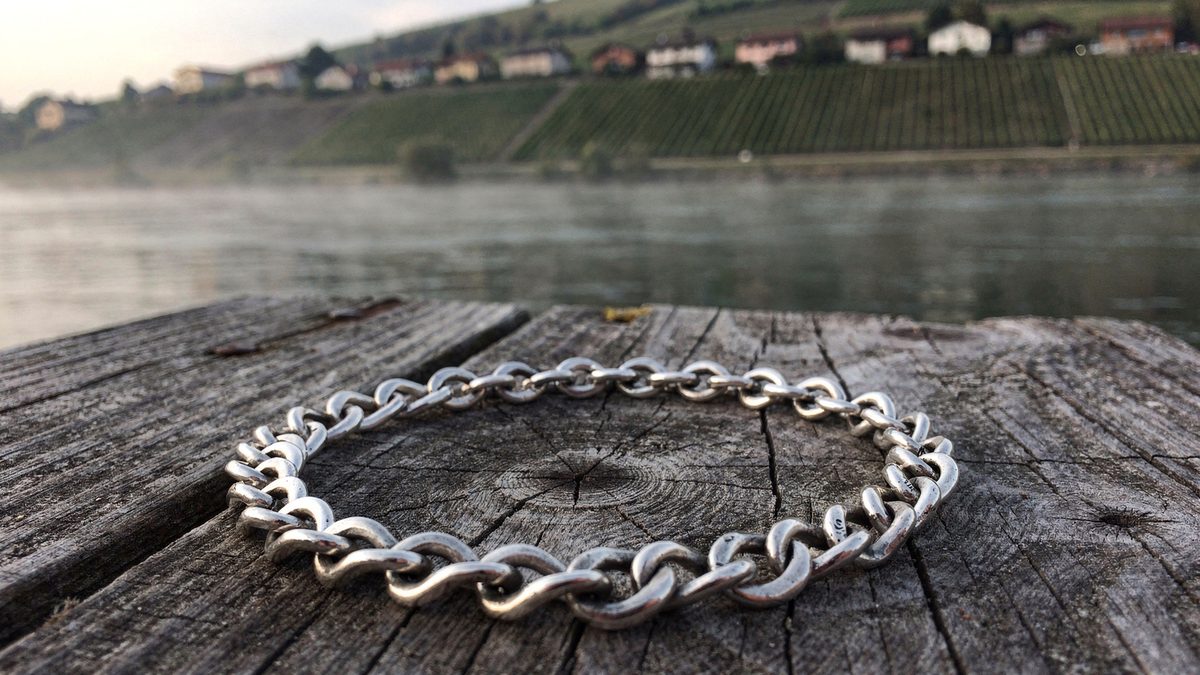 Un bracelet en argent sterling 925 posé sur les planches d’un ponton, la Moselle sous la brume et les coteaux de vigne en terrasses sur l’autre rive